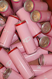 Pile of glossy light-pink 12 oz beverage cans in a box, red-rimmed tops with flavor labels like "crisp apple" and "raspberry lemon" visible