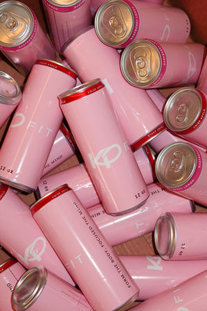 Pile of glossy light-pink 12 oz beverage cans in a box, red-rimmed tops with flavor labels like "crisp apple" and "raspberry lemon" visible