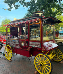 Bright vintage red-and-yellow popcorn cart with wooden wheels, striped awning and brass trim selling hot buttered popcorn on a tree-lined downtown brick sidewalk