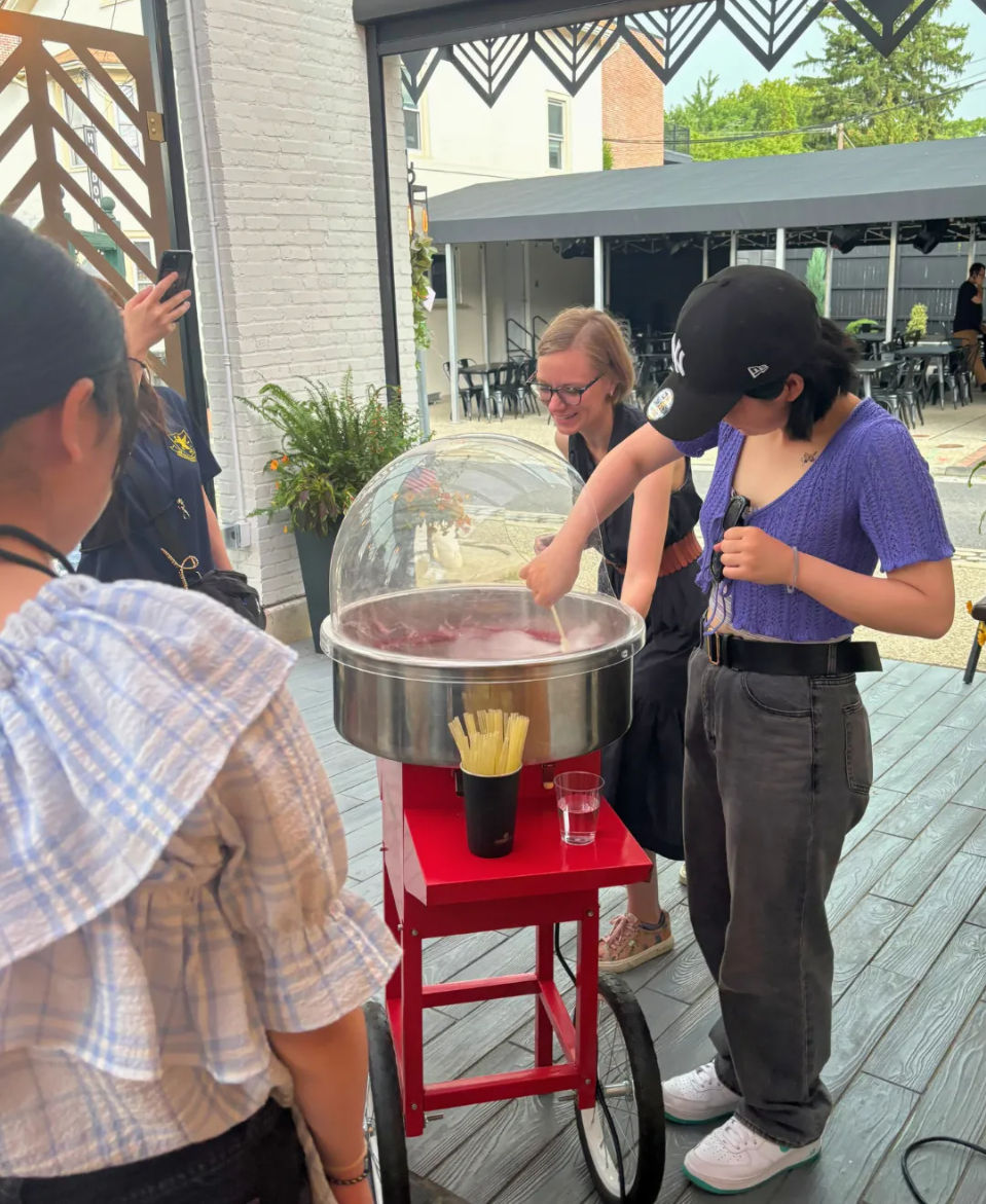 Group making pink cotton candy at a red wheeled cart on an outdoor patio with bistro tables and greenery