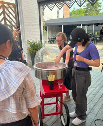 Group making pink cotton candy at a red wheeled cart on an outdoor patio with bistro tables and greenery