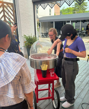 Group making pink cotton candy at a red wheeled cart on an outdoor patio with bistro tables and greenery