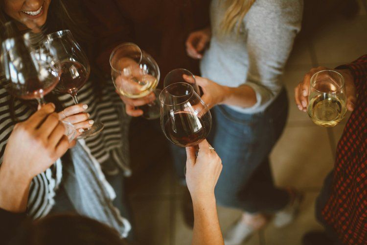 Top-down view of friends clinking red and white wine glasses in a cozy indoor gathering — casual wine toast and laughter.