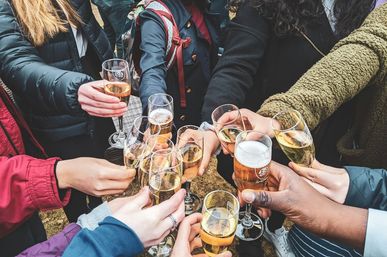 Many hands in jackets clinking champagne flutes and a beer glass in an outdoor celebration, a bubbly toast among a group.