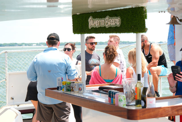 Group of people chatting around a bar on a sunny boat deck during a coastal cruise