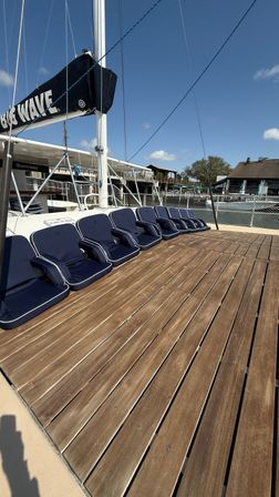 Sunny marina sailboat deck with wooden planks, row of navy cushioned seats and mast rigging against a clear blue sky