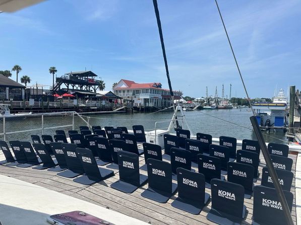 Rows of navy folding seats on a boat deck at a sunny coastal marina, overlooking calm harbor waters, sailboats, palm trees and waterfront restaurants.