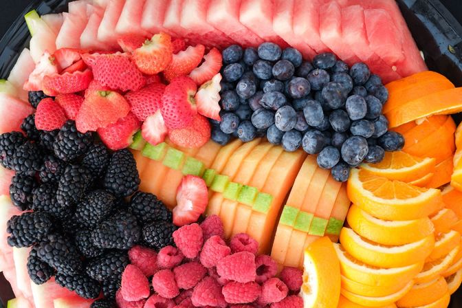 Vibrant fresh fruit platter with sliced watermelon, cantaloupe, orange wedges and piles of blueberries, strawberries, blackberries and raspberries