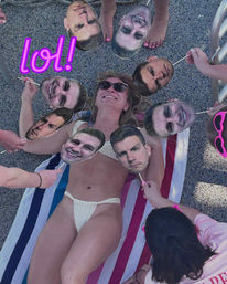 Woman in white bikini and sunglasses lying on a striped beach towel poolside, smiling as friends surround her holding oversized cardboard face cutouts on sticks in a playful scene with pink accessories and a “lol” graphic.