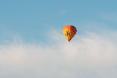 Orange hot air balloon with cactus graphic drifting above a layer of white clouds against a clear blue sky