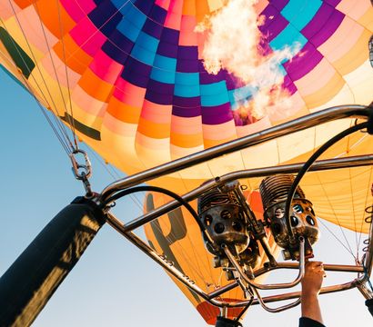 Vibrant hot air balloon canopy and burner flame seen from the basket during a sunrise ride over a desert plain with distant mountain range.