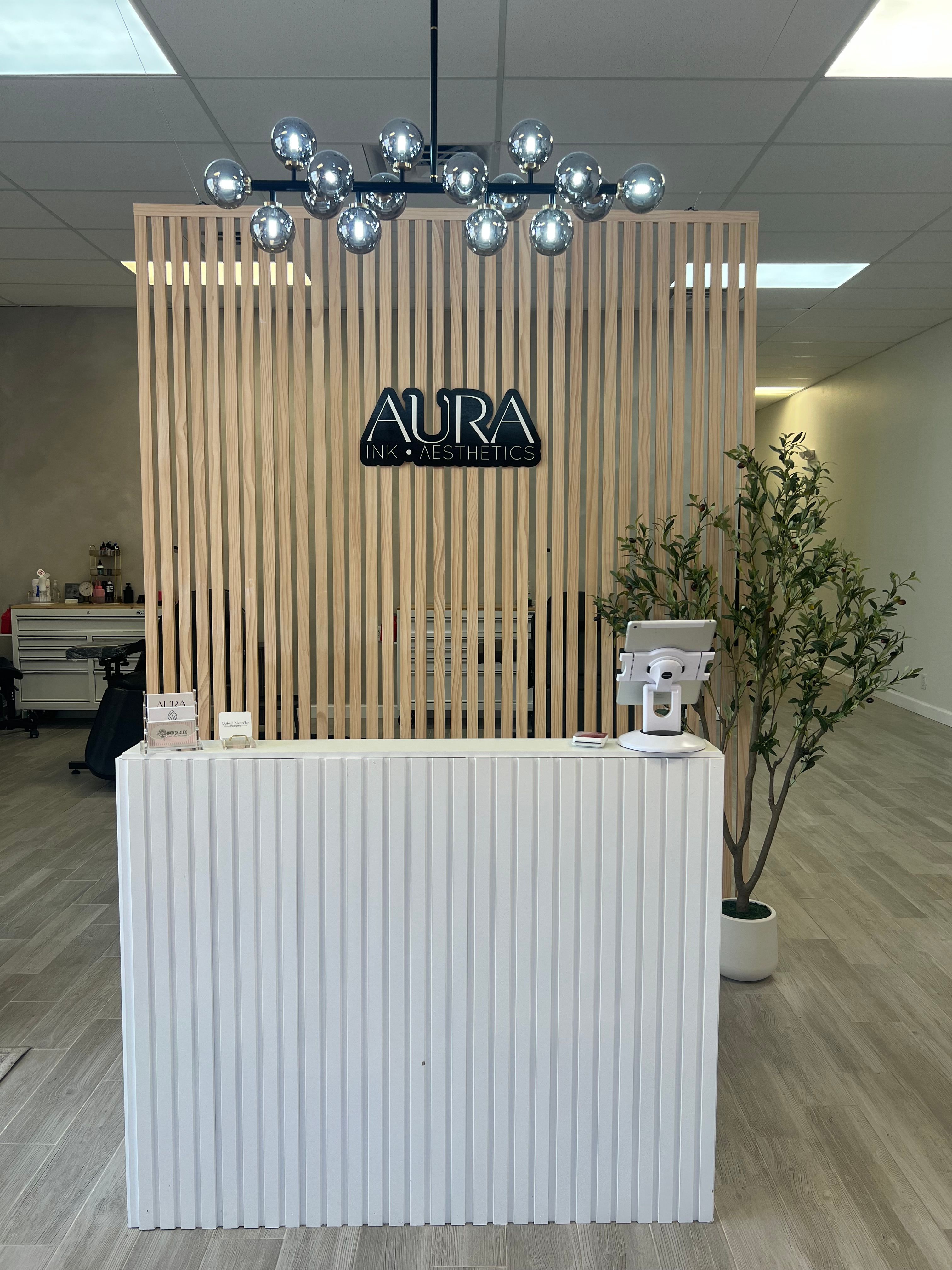 Minimalist spa reception with light wood slatted partition, chrome globe chandelier, white ribbed front desk and a potted plant in a bright, modern clinic lobby