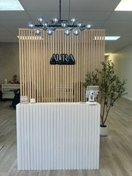 Minimalist spa reception with light wood slatted partition, chrome globe chandelier, white ribbed front desk and a potted plant in a bright, modern clinic lobby