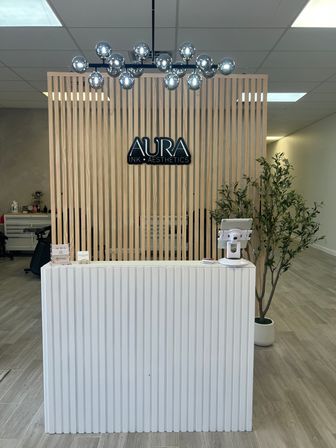 Minimalist spa reception with light wood slatted partition, chrome globe chandelier, white ribbed front desk and a potted plant in a bright, modern clinic lobby