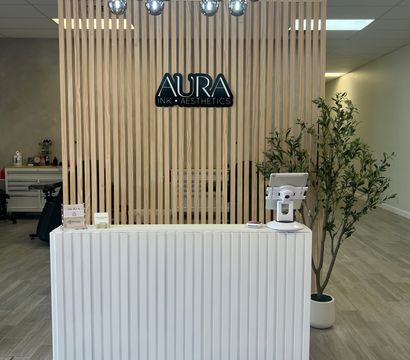 Minimalist spa reception with light wood slatted partition, chrome globe chandelier, white ribbed front desk and a potted plant in a bright, modern clinic lobby