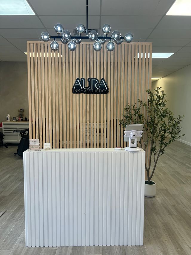 Minimalist spa reception with light wood slatted partition, chrome globe chandelier, white ribbed front desk and a potted plant in a bright, modern clinic lobby