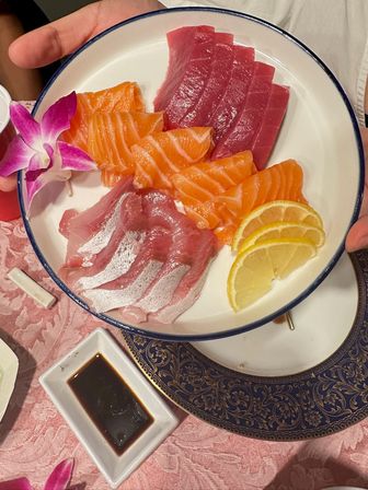 Colorful sashimi platter of sliced tuna, salmon and white fish with lemon wedges and a purple orchid on a white rimmed plate, soy sauce dish on the table — fresh Japanese sashimi