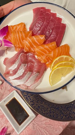 Vibrant Japanese sashimi plate with neatly sliced tuna, salmon and white fish, lemon wedges and a purple orchid garnish, served with soy sauce on decorative dinnerware.