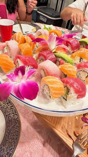 Colorful rainbow sushi platter with salmon, tuna and avocado rolls, purple orchid garnishes and chopsticks on a festive dinner party table with red cups