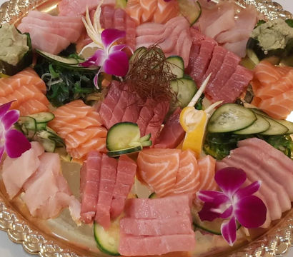 Vibrant Japanese sashimi platter on a gold tray with sliced salmon, tuna and whitefish, cucumber, seaweed salad, wasabi, lemon and purple orchid garnishes