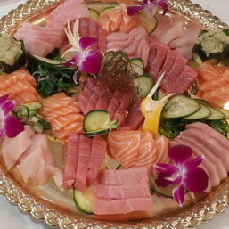 Colorful Japanese sashimi platter with sliced salmon, tuna and white fish on a decorative gold tray, garnished with cucumber, seaweed, wasabi and purple orchid flowers