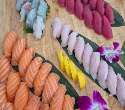 Vibrant sushi nigiri platter on a wooden board—rows of salmon, tuna and white-fish nigiri with lemon slices and purple orchid garnishes