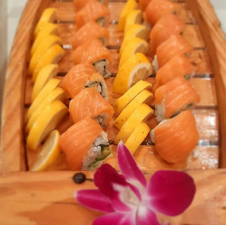 Fresh salmon-topped sushi rolls lined with lemon wedges on a wooden boat platter, garnished with a purple orchid – bright Japanese cuisine presentation.