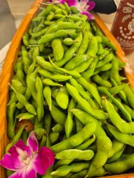 Close-up of bright green edamame pods piled in a wooden tray, lightly salted and garnished with a purple orchid.