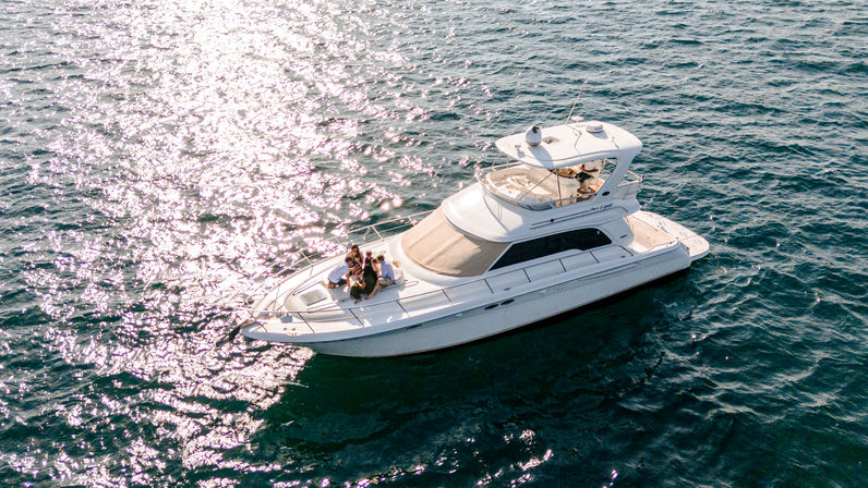 Aerial view of a white luxury yacht on sparkling blue ocean water with a small group of people lounging on the bow on a sunny day