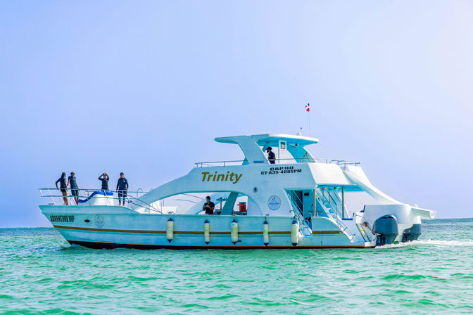 White double-decker catamaran tour boat with passengers on deck cruising turquoise tropical ocean under a clear blue sky