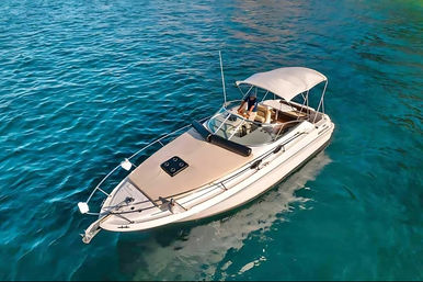 Aerial view of a white motorboat with bimini top and cushioned sun deck floating in clear turquoise coastal waters