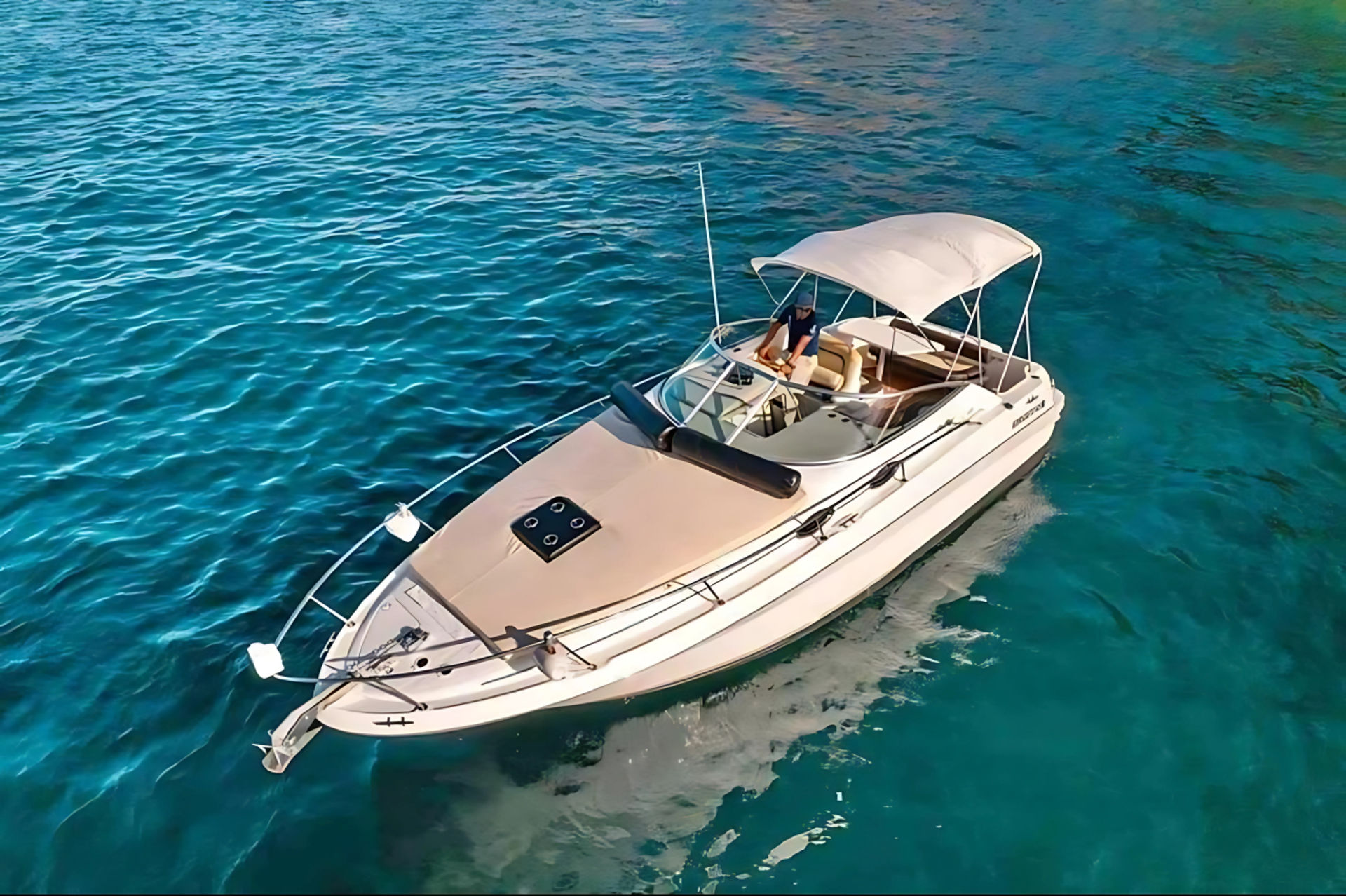 Aerial view of a white motorboat with bimini top and cushioned sun deck floating in clear turquoise coastal waters