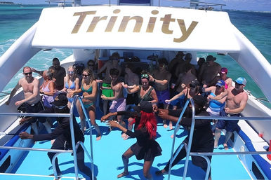 Lively daytime boat party on a sunlit deck over turquoise water, dancers leading a crowd of vacationers enjoying music and drinks