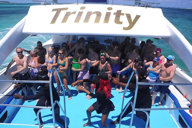 Lively daytime boat party on a sunlit deck over turquoise water, dancers leading a crowd of vacationers enjoying music and drinks