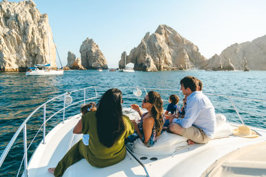 Group of people relaxing on a yacht near the dramatic rock arches of Cabo San Lucas, Mexico, with sailboats on turquoise sea and clear blue sky
