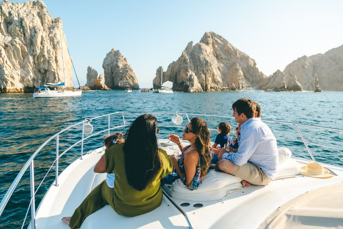 Group of people relaxing on a yacht near the dramatic rock arches of Cabo San Lucas, Mexico, with sailboats on turquoise sea and clear blue sky
