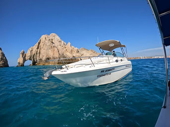 White motorboat bobbing on turquoise sea in front of Cabo San Lucas iconic rock arch under a cloudless blue sky