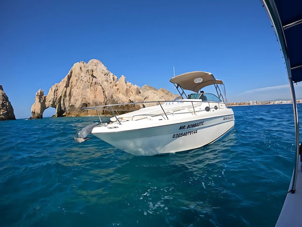 White motorboat bobbing on turquoise sea in front of Cabo San Lucas iconic rock arch under a cloudless blue sky