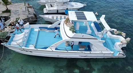 White luxury party yacht with turquoise deck and pastel green and gold balloon decorations, crew in white preparing at a tropical marina dock over clear turquoise water