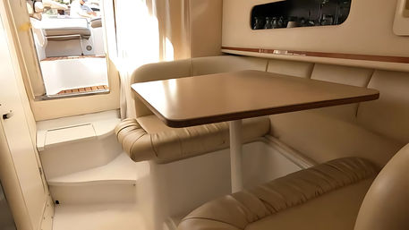 Cozy beige leather dinette in a boat cabin — compact table with U-shaped seating and steps up to a sunlit cockpit.