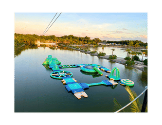 Aerial view of a colorful inflatable water park course floating on a tropical lagoon surrounded by palm trees at sunset