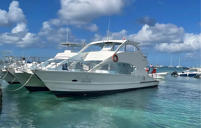 White motor yacht moored at a sunny tropical marina with clear turquoise water, puffy blue sky, and other boats in the background.