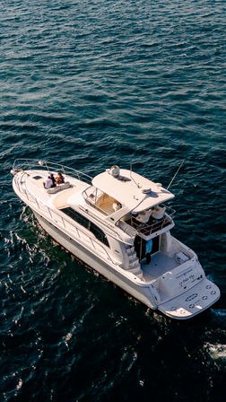 Aerial view of a sun-soaked white luxury yacht cruising the deep blue ocean with people relaxing on the bow