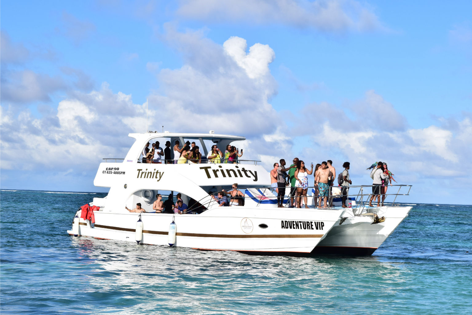 White double-decker tour boat with groups of people enjoying sunny tropical turquoise ocean under a bright blue sky.