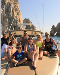 Smiling group lounging on a boat bow with the El Arco rock formation at Cabo San Lucas, Mexico, under clear blue skies