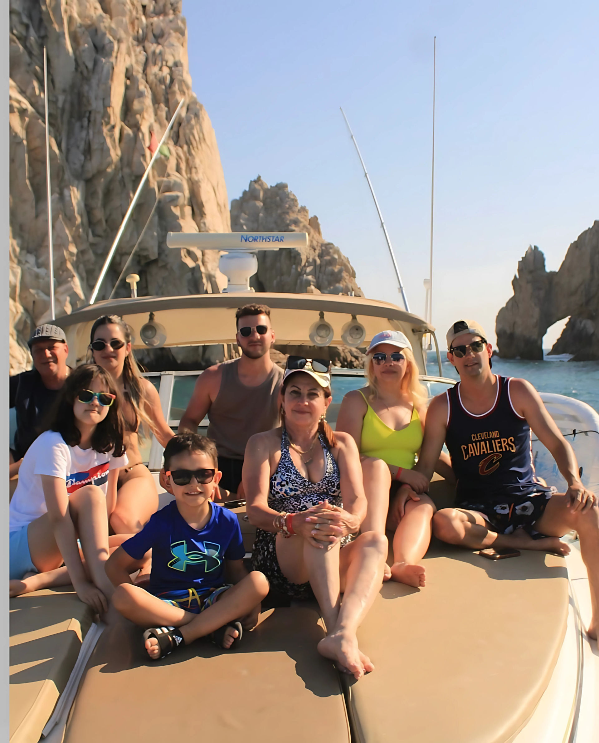 Smiling group lounging on a boat bow with the El Arco rock formation at Cabo San Lucas, Mexico, under clear blue skies