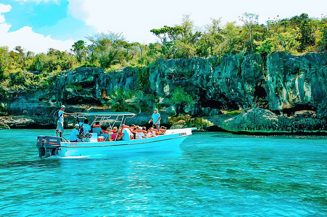 Tour boat with passengers cruising vibrant turquoise water past rugged limestone cliffs and lush tropical shoreline.