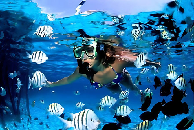 Snorkeler wearing a mask and snorkel glides through clear turquoise water, playfully surrounded by dozens of black-and-white striped tropical fish above a shallow reef.