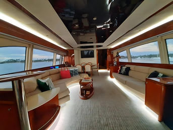 Luxury yacht salon with cream leather sofas, glossy wood trim and ambient LED lighting, panoramic windows overlooking a calm coastal marina at sunset.