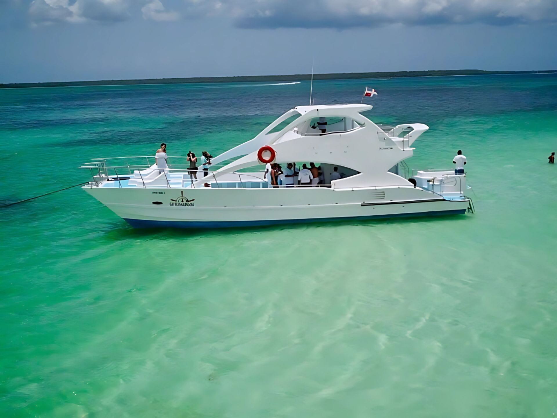 White luxury yacht anchored in shallow turquoise tropical lagoon, passengers on deck enjoying clear sea and a partly cloudy sky